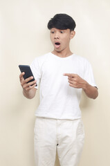 Fototapeta premium Handsome Asian guy in studio looks surprised at screen of mobile phone