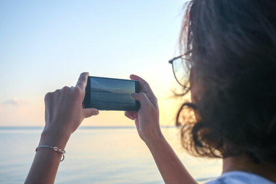 Woman taking pictures of beach, sea and resort at sunrise He used his phone to take high-angle shots. Travel concept and technology