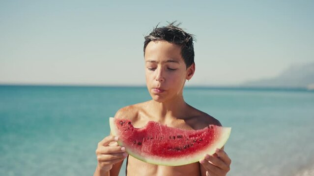  Boy eating watermelon on the beach, summertime.