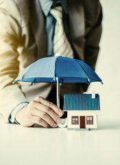 An insurance agent is holding a blue umbrella over a modern house model. Property insurance...