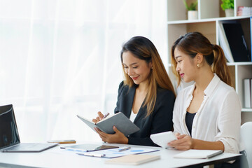 Two Asian business women discuss working together in the office.