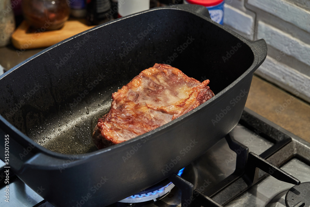 Wall mural Piece of meat is roasted in rectangular pot for cooking over fire on gas stove