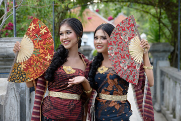 Beautiful girls in Balinese traditional costume with a fan, in the gardens of Taman Ujung Bali.