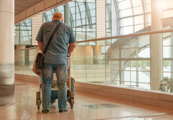 A full-length figure of a man in blue jeans and a shirt, with a luggage cart, against the background of the airport interior, a copy of the space on the right
