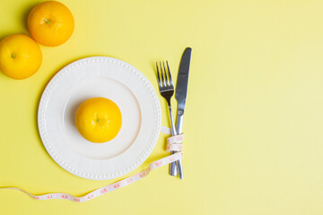 Diet concept with orange on a white plate with fork and knife over the yellow background.