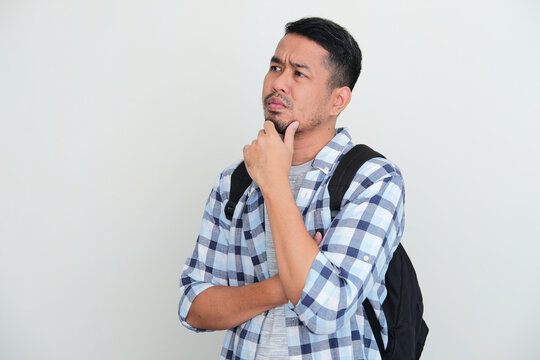 Adult Asian man wearing backpack waiting for someone to come with unsure expression