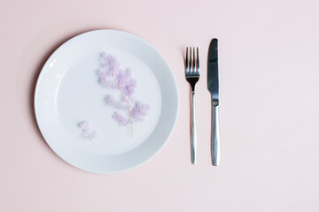 Diet concept with purple flowers over the white plate with fork and knife over the pink background. 