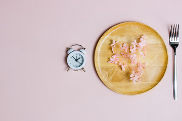 Diet concept with clock, wooden plate and fork over the pink background. 