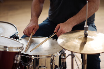 Close-up of man sitting behind drum kit and playing drums during rehearsal