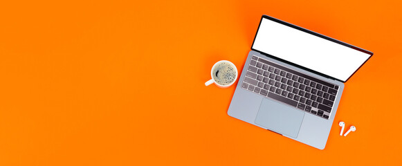 Laptop with blank screen, cup of coffee and wireless headphones on orange background