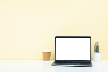 Laptop with blank screen, paper cup and cactus on white table