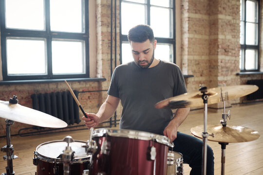 Young bearded man sitting at drum kit and performing on drums at studio during rehearsal