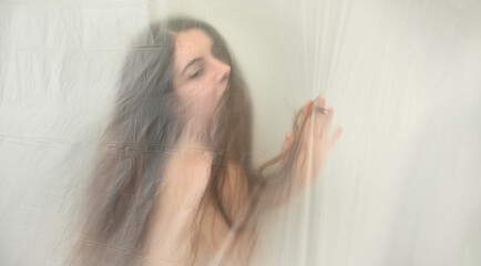 blurred, fuzzy image of sensual romantic young naked woman portrait behind plastic film, looking...