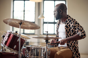 Serious African drummer recording music sitting at drums set during rehearsal