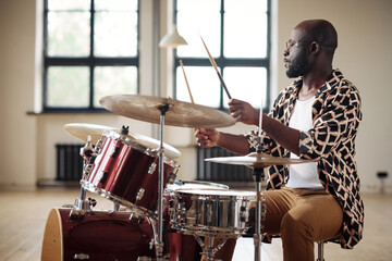African drummer practicing to play drums sitting at drums set at studio