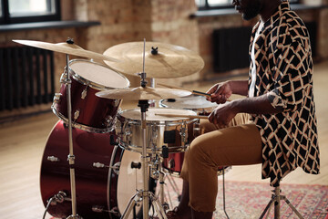 African musician playing at drums set with drumsticks at empty studio