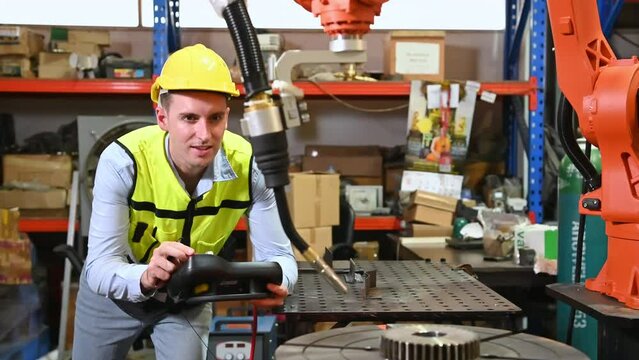 A male worker is controlling a welding robot. by using forcing welding with a control screen which is used for precision welding control. Fast and highly secure