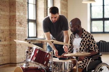 African young man with disability learning to play drums with drummer teaching him at studio