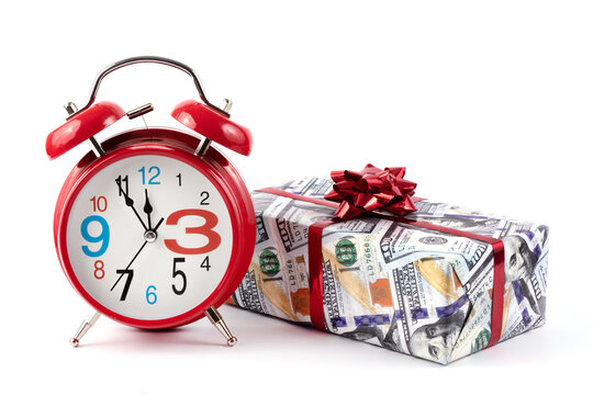 Red alarm clock and a gift box wrapped in paper with a picture of 100 american dollars bills on a white background