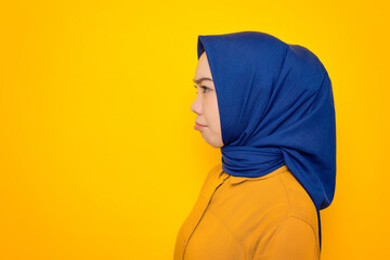 Unhappy young Asian Muslim woman dressed in orange looking aside at copy space isolated on yellow background