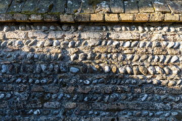 Particolare di antico muro di pietra e mattoni. Muro di recinzione metà illuminato dal sole e metà in ombra.