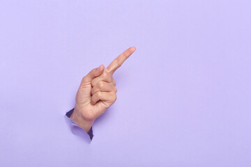 Person's hand breaking through lilac paper wall demonstrates copy space for your promotional...