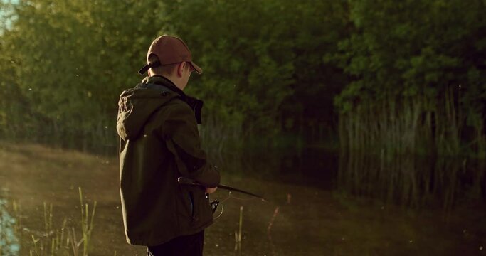 schoolboy is fishing alone by shore beautiful pond or river in early morning, 4K, Prores