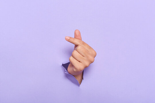 Human's hands showing symbol korean mini heart gesure through the torn holes of purple paper background. Creative art, copy space.