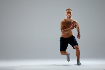 Developing endurance. Male athlete in motion isolated over gray studio background. Maintaining health and strength. Concept of sport, healthy lifestyle, motion