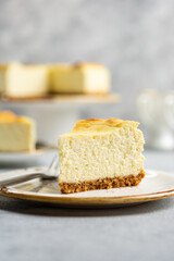 A piece of vanilla cottage cheese cheesecake on a shortbread on a ceramic plate on a light concrete background. Close-up.