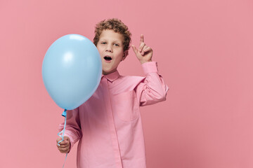 a beautiful cute little school-age boy stands with a blue balloon in his hand and emotionally poses...