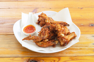 Fried chicken wing with chilli sauce in white plate on brown wooden table.