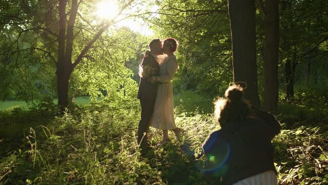 professional photographer takes pictures of beautiful loving couple of husband and wife at sunset. process of photographing bride and groom in park in rays of dawn sun.
