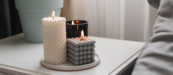 Modern burning candle on bedside table near bed. Home aroma. Wellness. Banner image for design