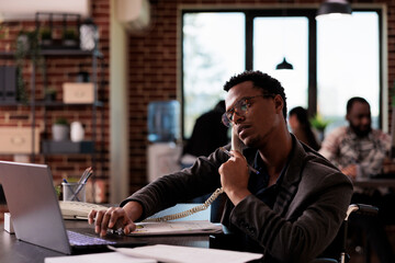 Company employee with physical disability talking on landline phone call, using office telephone at...