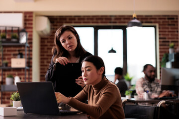 Fototapeta premium Asian woman with physical impairment brainstorming ideas with manager, paralyzed wheelchair user doing teamwork. Entrepreneur with health condition working in disability friendly office.