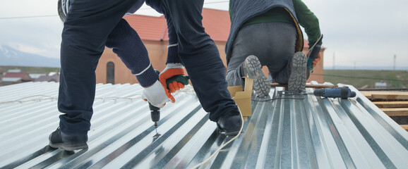 Man installing metal sheet roof by electrical drilling machine.