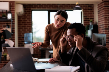 Businessman with impairment analyzing website app on laptop, working with colleague in disability friendly office. Male employee wheelchair user with health condition doing teamwork strategy.