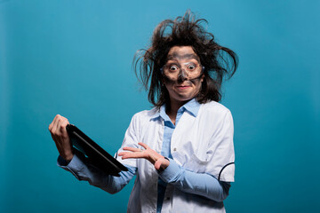 Mad chemist having touchscreen tablet and confused expression with messy hair and dirty face after...