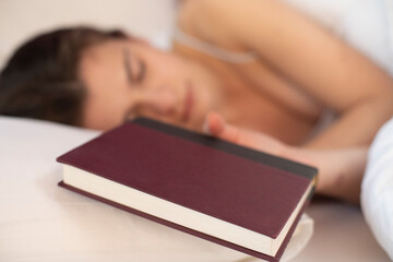 Young woman in bed sleeping with a book in hand.