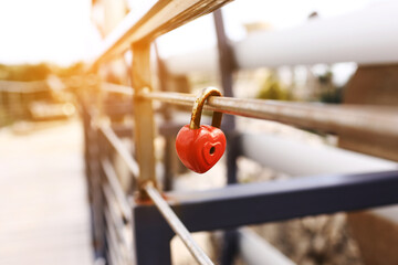 The lock hangs on the metal fence. Symbol of love in the park. The metal red lock in the shape of a...