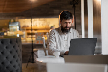 Fototapeta premium Young bearded man working in cafe using laptop, freelancer work man with pc in coffee shop