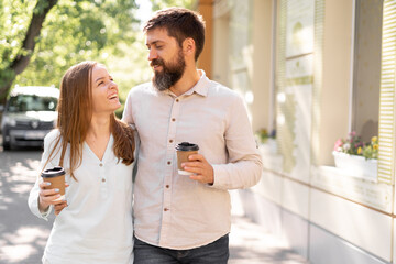 young smiling couple with takeaway coffee walk in summer enjoying conversation while toothy smiling and looking at each other, relationship and lifestyle concept