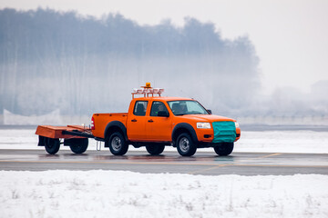 Airport service car on runway on airfield during snowfall