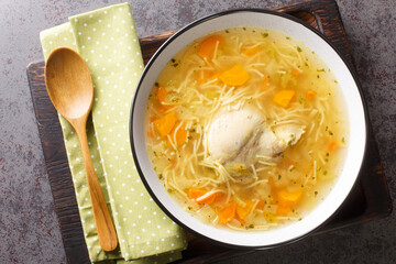 Delicious homemade chicken broth with noodles and vegetables close-up in a plate on a wooden tray....