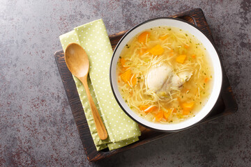 Polish Rosol z kury chicken soup with vermicelli and vegetables close-up in a bowl on a wooden tray on the table. horizontal top view from above