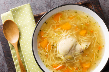 Dietary chicken soup with vermicelli and vegetables close-up in a bowl on a wooden tray on the table. horizontal top view from above © FomaA