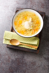 Light chicken soup with pasta and vegetables close-up in a bowl on a wooden tray on the table. Vertical top view from above © FomaA