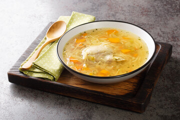 Delicious homemade chicken broth with noodles and vegetables close-up in a plate on a wooden tray. horizontal © FomaA