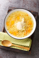 Chicken broth with noodles and vegetables close-up in a plate on a wooden tray. Vertical top view from above © FomaA